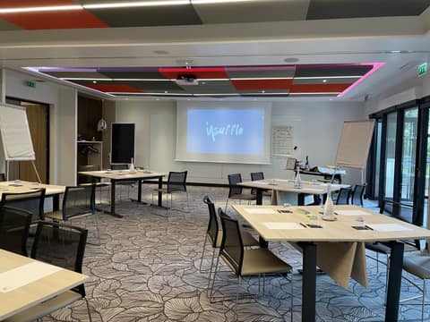 Salle de séminaire vide installée en îlots de tables, feuilles et verres à chaque place, deux paperboards, un agenda manuscrit au mur et le logo Insuffle projeté sur l'écran.